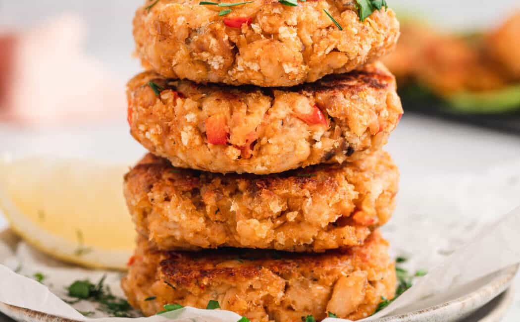 A stack of four canned salmon patties on a small white plate.