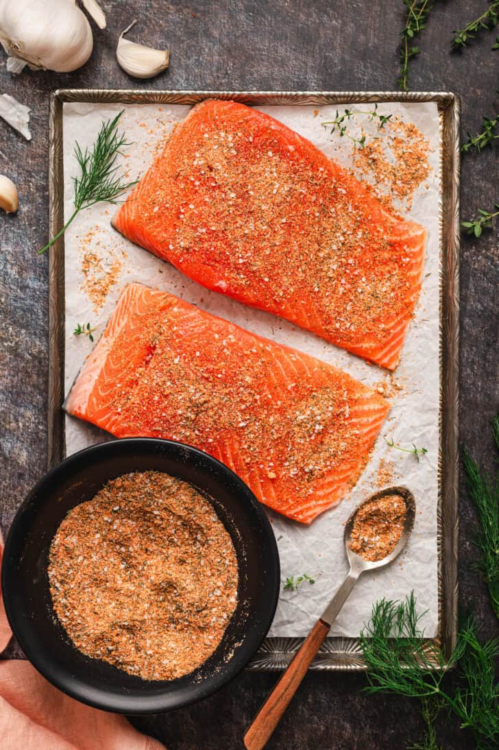 A rimmed baking pan with two pieces of raw fish and a bowl of a salmon seasoning recipe.