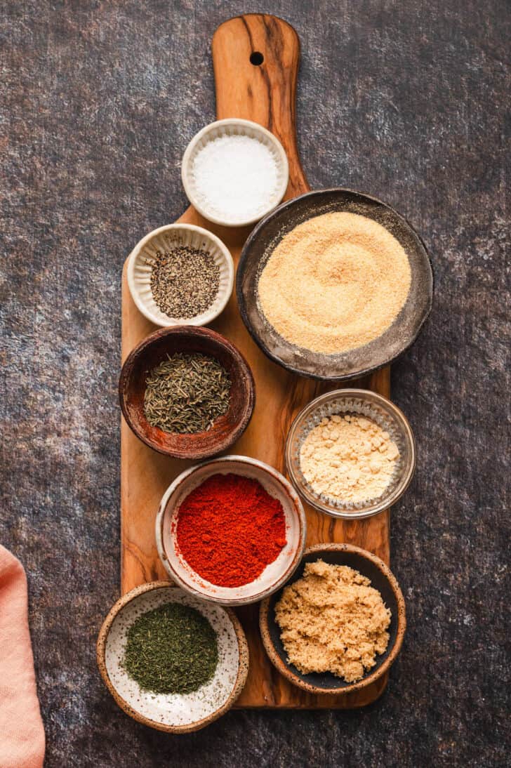 Bowls filled with dried herbs and spices on a wooden cutting board.