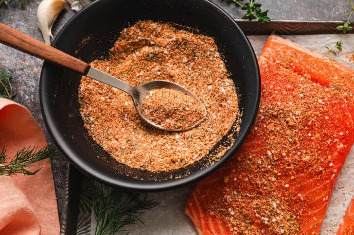 A black bowl filled with the best seasoning for salmon with a spoon in it.