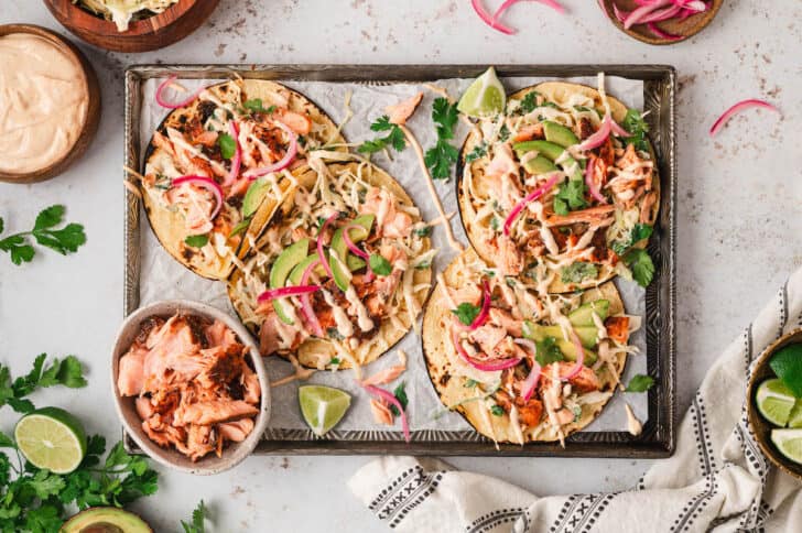 Salmon fish tacos on a parchment-lined rimmed baking pan.