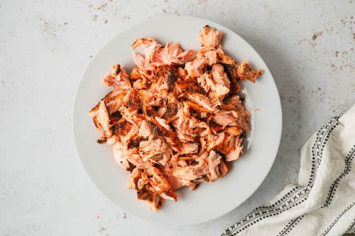 Cooked salmon broken into chunks on a white plate.