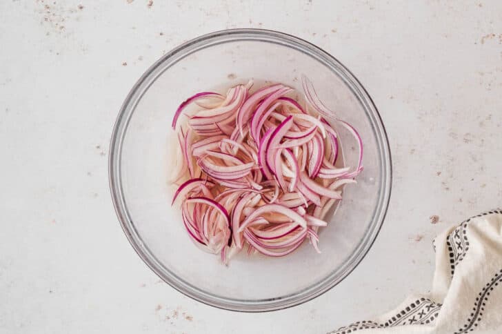 A glass bowl filled with sliced red onions in a pickling mixture.