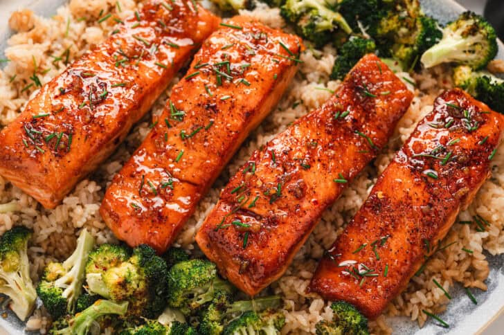 Four pieces of a honey salmon recipe on a platter, served over rice and broccoli.