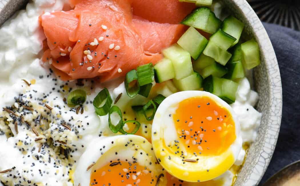 Gray bowl filled with cottage cheese, soft egg, smoked salmon and green onions.