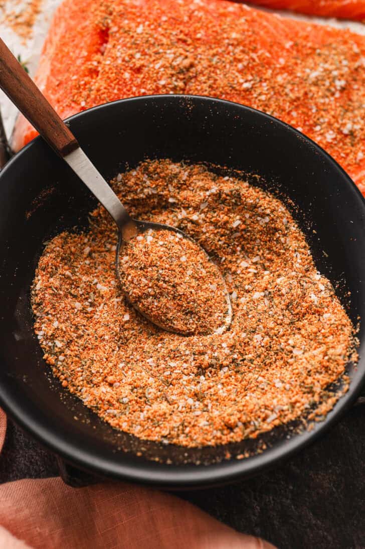 A black bowl filled with seasoning for salmon with a spoon in it.