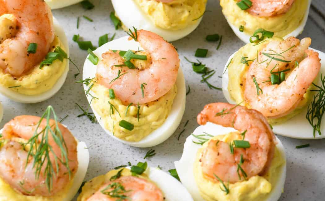 Shrimp deviled eggs garnish with chives and dill on a light gray plate.