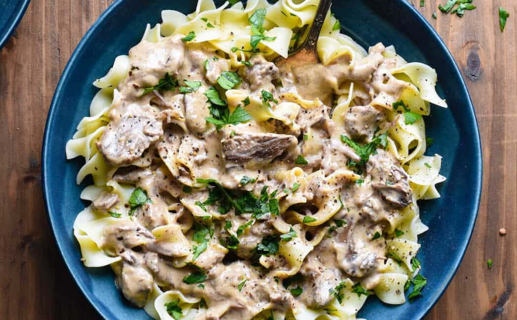 Blue ceramic bowl filled with slow cooker beef stroganoff served over egg noodles.