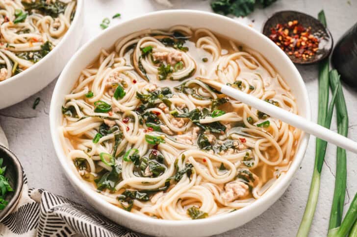 A shallow white bowl filled with pork noodle soup, with a spoon in it.