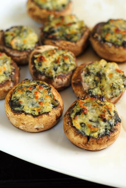 Closeup photo of spinach-dip stuffed mushrooms on white platter.