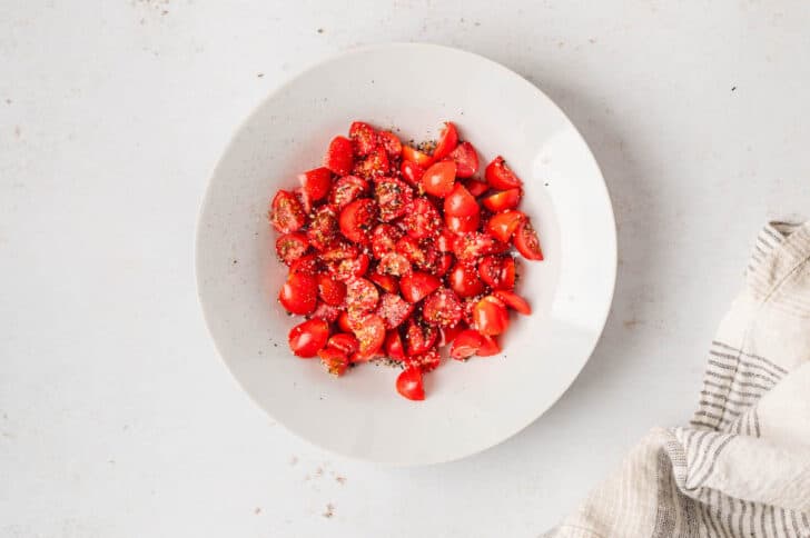 A white bowl filled with quartered grape tomatoes, sprinkled with salt and pepper.