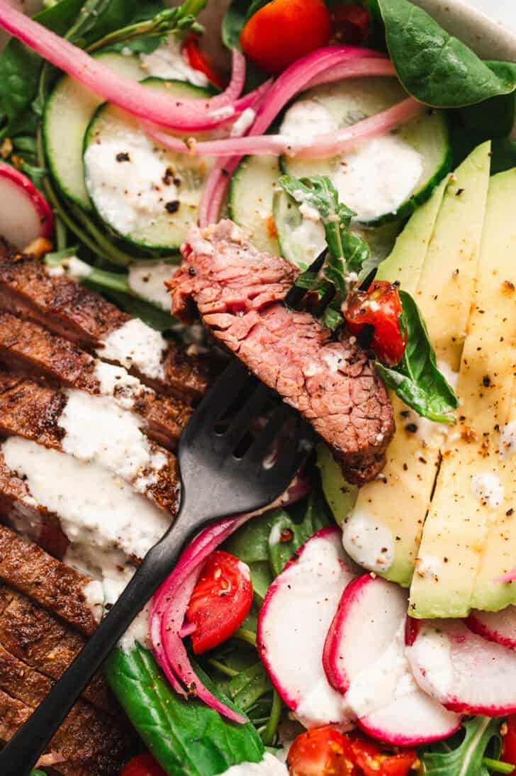 A closeup of a fork skewering a piece of meat in a salad with steak recipe.