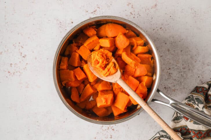 A wooden spoon scooping cooked yams out of a pot.