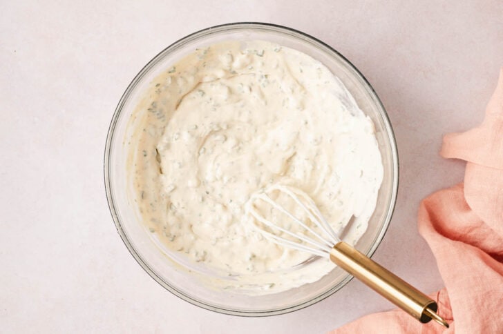 A glass bowl filled with a creamy sauce, with a whisk in it.