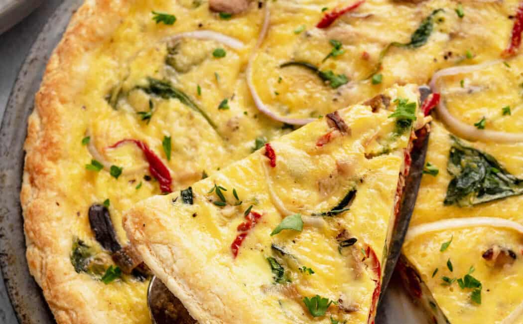 A slice of vegetarian quiche being lifted out of a full quiche in a metal pie plate.